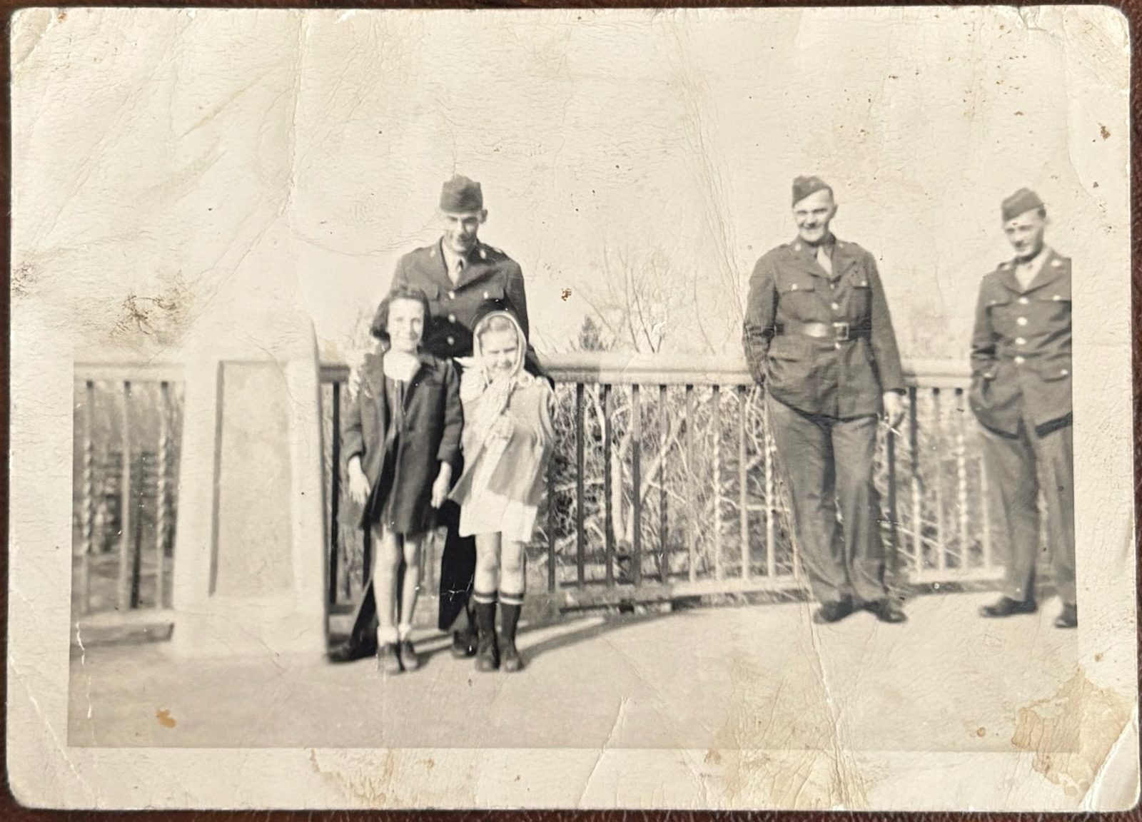 Soldiers with two young girls on an ornate iron bridge — a furlough visit with family (winter, bare trees).