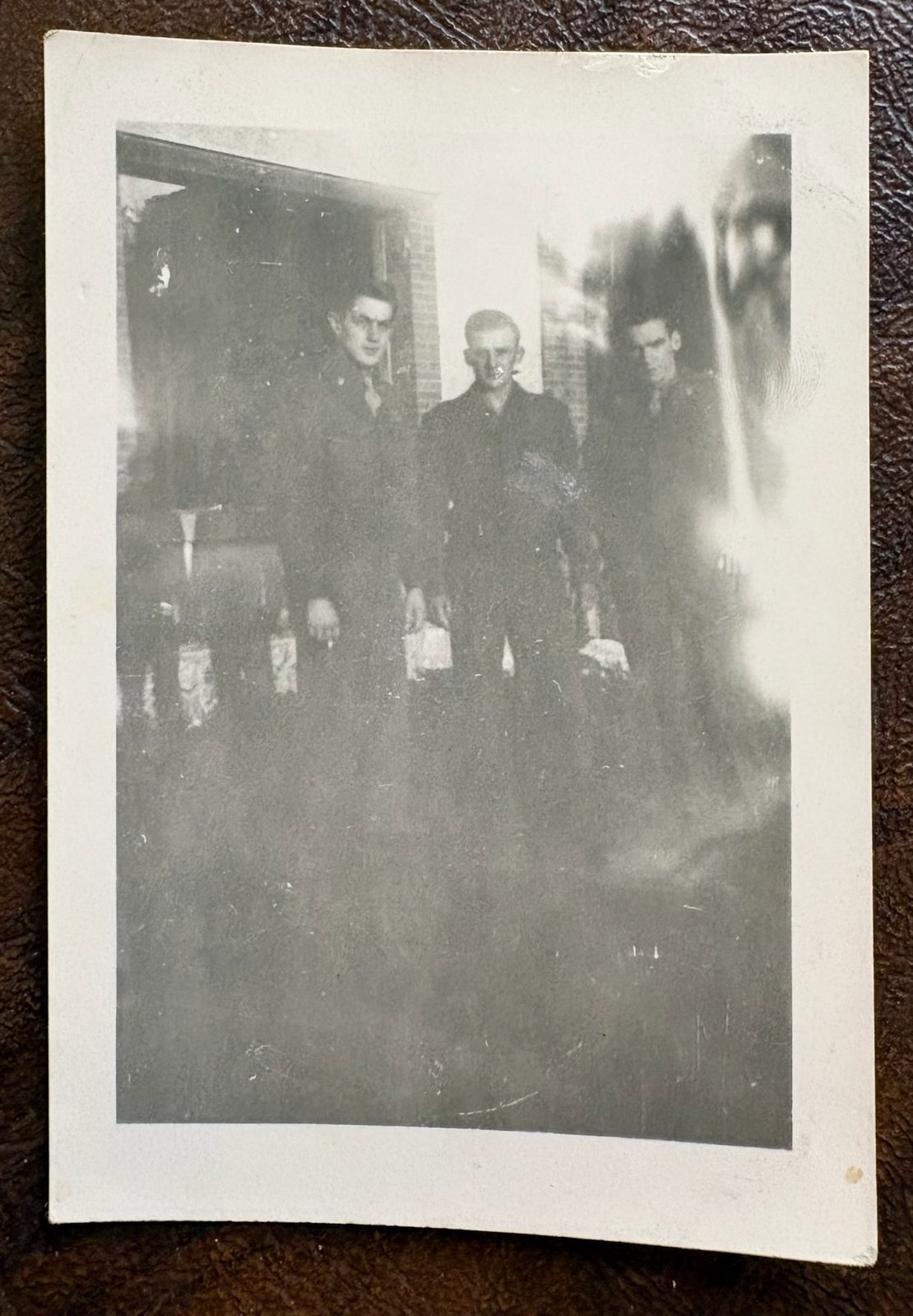 Three soldiers by a brick building (light-leaked print).